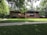 A brick house with a low-pitched roof surrounded by lush greenery and a well-maintained lawn. There are vibrant flowers planted in large planters near the entrance, and the architecture features horizontal lines and large windows.