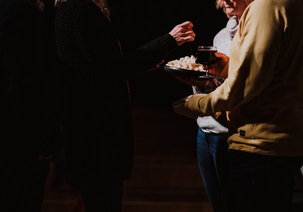 three person standing and holding glass of wine and food