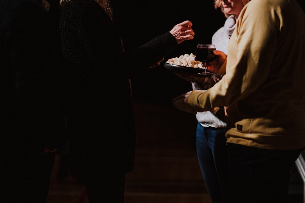 three person standing and holding glass of wine and food