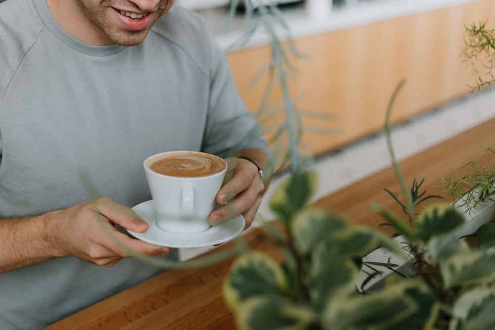 shallow focus photo of person holding white ceramic mug and saucer