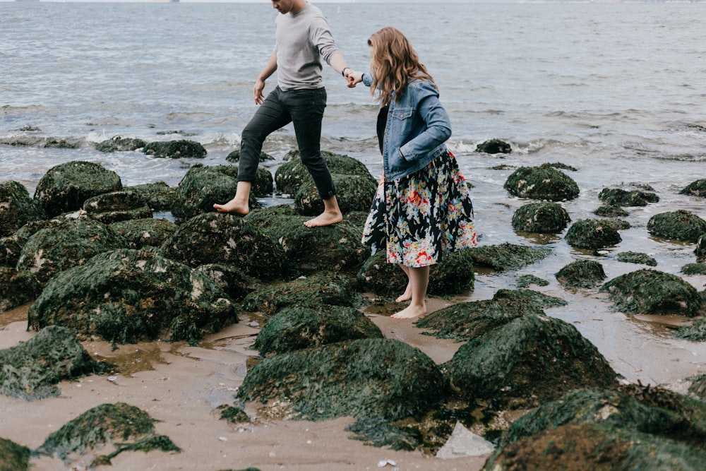 man and woman holding hand together while stepping on rocks near sea