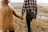 Happy couple walking hand-in-hand along a rustic farmhouse driveway surrounded by fields