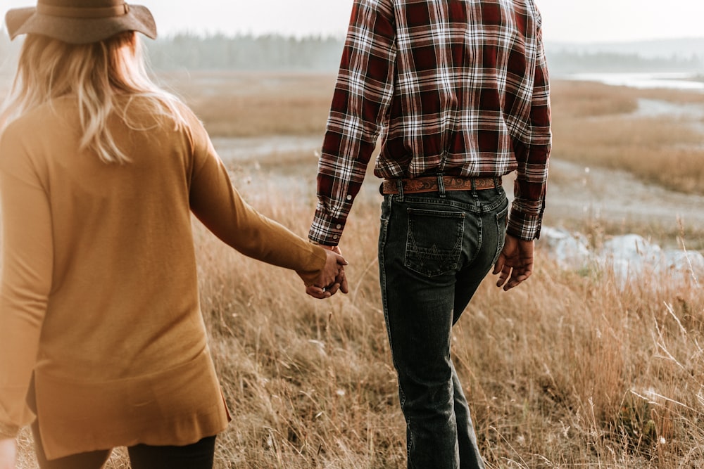 uomo e donna che camminano lungo il campo d'erba mentre si tengono per mano