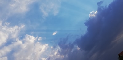 A dynamic sky is filled with a blend of bright blue and dark, dramatic clouds. The lighter clouds are fluffy and scattered, gradually transitioning to a darker, more ominous shade on the right, suggesting an incoming storm.