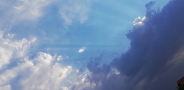 A dynamic sky is filled with a blend of bright blue and dark, dramatic clouds. The lighter clouds are fluffy and scattered, gradually transitioning to a darker, more ominous shade on the right, suggesting an incoming storm.
