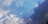 A dynamic sky is filled with a blend of bright blue and dark, dramatic clouds. The lighter clouds are fluffy and scattered, gradually transitioning to a darker, more ominous shade on the right, suggesting an incoming storm.