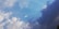A dynamic sky is filled with a blend of bright blue and dark, dramatic clouds. The lighter clouds are fluffy and scattered, gradually transitioning to a darker, more ominous shade on the right, suggesting an incoming storm.
