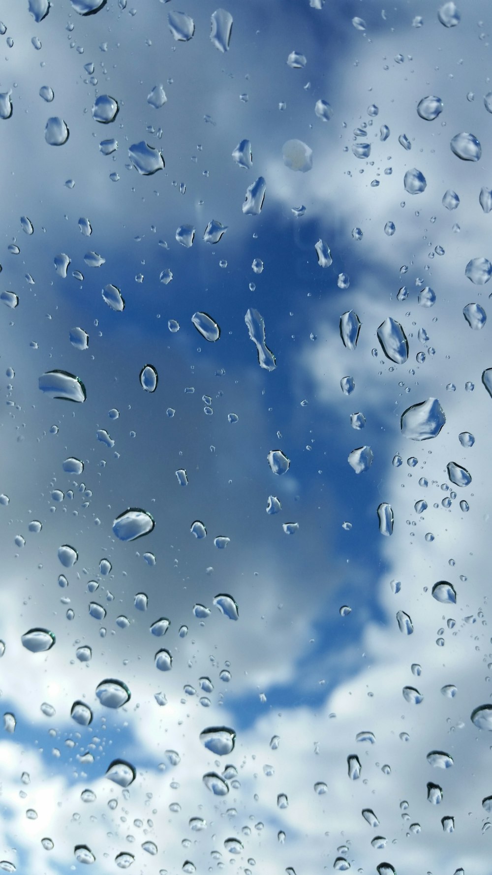 Regentropfen auf ein Fenster mit blauem Himmel im Hintergrund