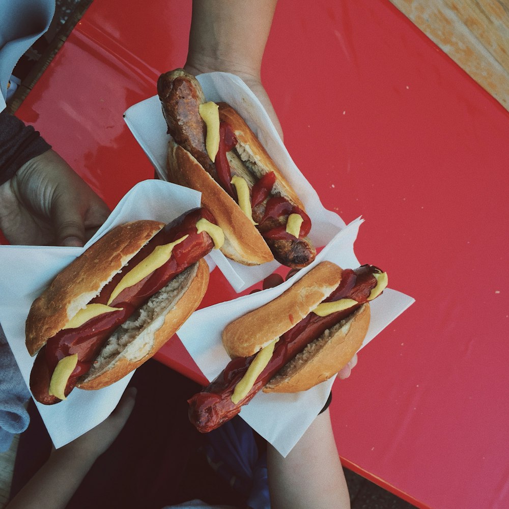 Tres personas sosteniendo panecillos de perritos calientes