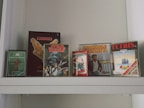 Several retro video game boxes are displayed on a shelf. The collection includes titles such as World Cup Football, Star Wars, Impossible Mission II, Tetris, and Ghostbusters. The games appear to be for older gaming systems, indicated by the distinctive box designs and logos.