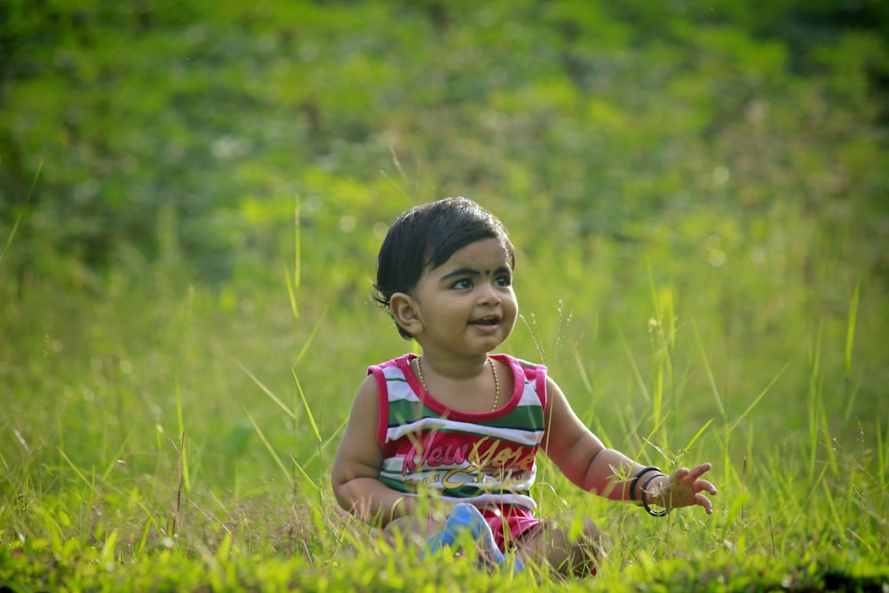 boy in multicolored tank top sits on green grass