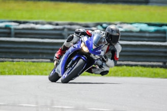 A close-up of a professional motorcycle racer wearing a reinforced racing suit, leaning into a sharp turn on a sunny racetrack.
