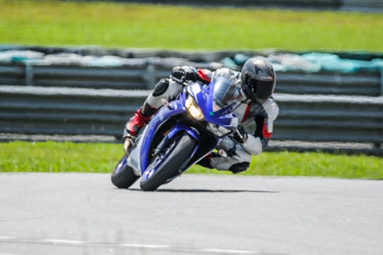A close-up of a professional motorcycle racer wearing a reinforced racing suit, leaning into a sharp turn on a sunny racetrack.