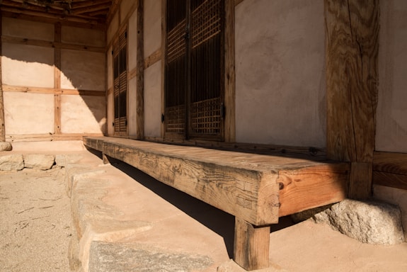 A traditional wooden structure with rustic wood beams and sliding lattice doors. The building's exterior is made of natural materials, with a smooth, earthy wall and a simple wooden bench on a stone platform.