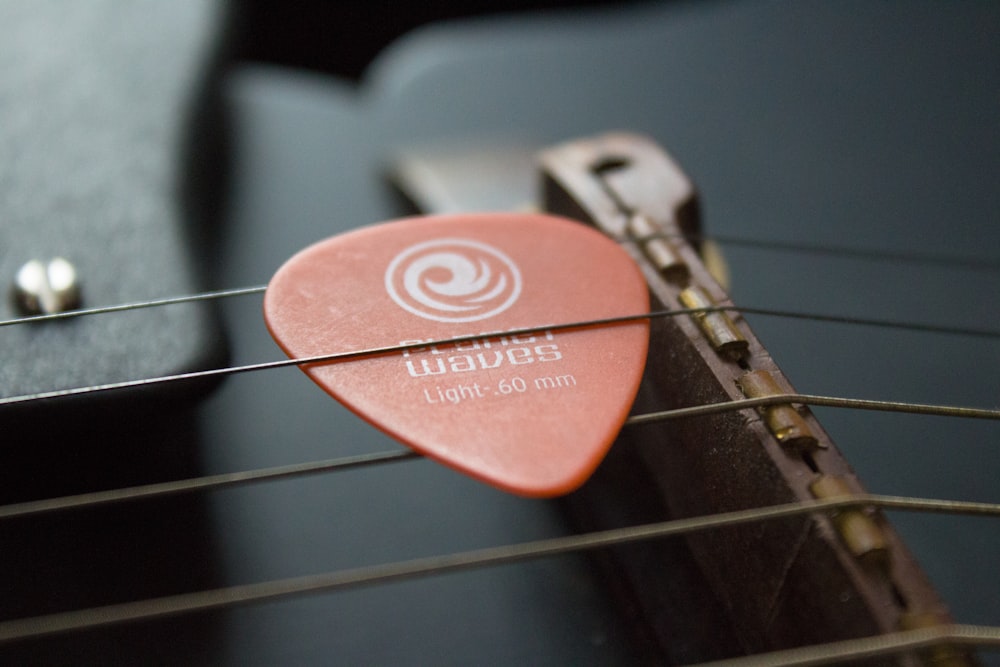 Fotografía de enfoque selectivo de púa de guitarra marrón en cuerdas de guitarra