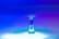 A vibrant and visually captivating water droplet captured in mid-air with a smooth reflective surface below. The colors range from deep blue to purple and teal, creating a mesmerizing transition of hues. The background is softly blurred, emphasizing the droplet in the foreground.