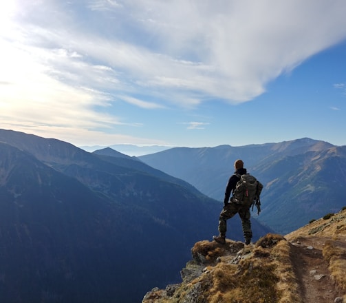 man on top of mountain under blue sky