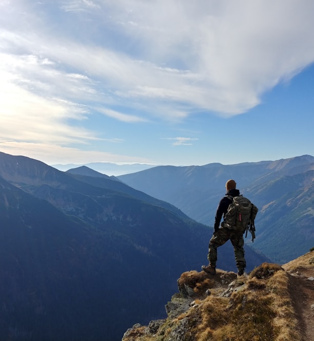 man on top of mountain under blue sky