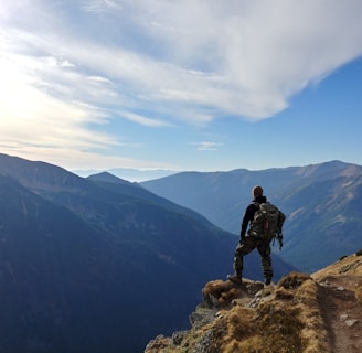 man on top of mountain under blue sky