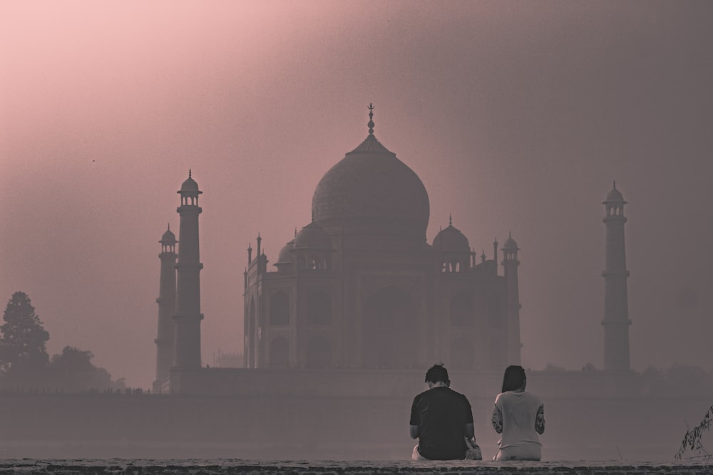 two man and woman sitting on pavement facing on buildings ahead