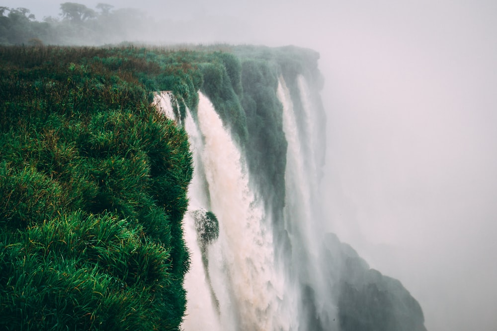 water falls with green field under foggy weather