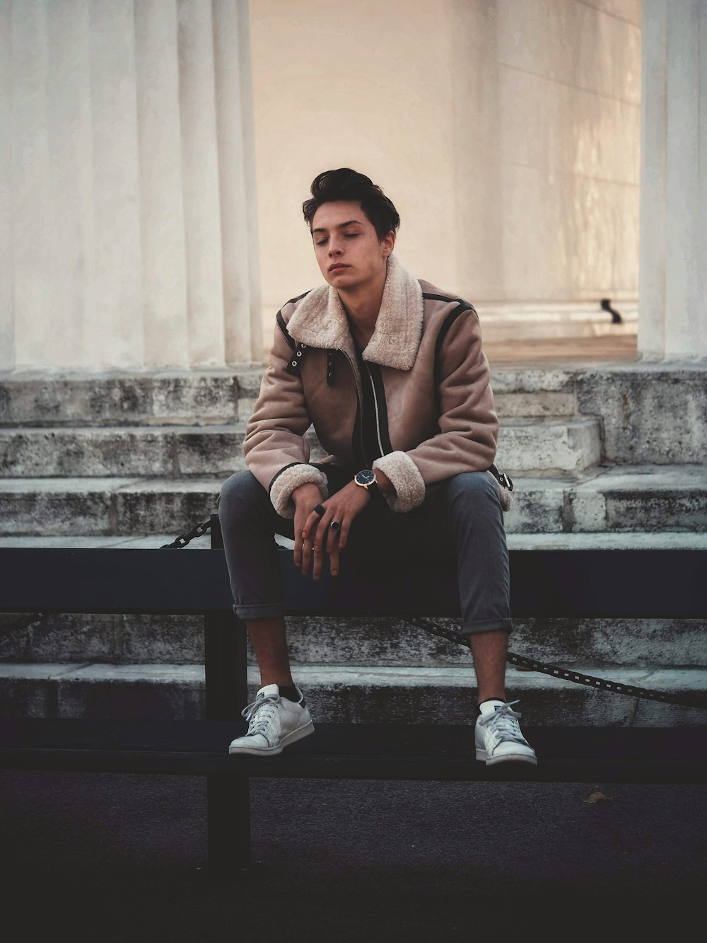 man wearing brown jacket sitting on fence