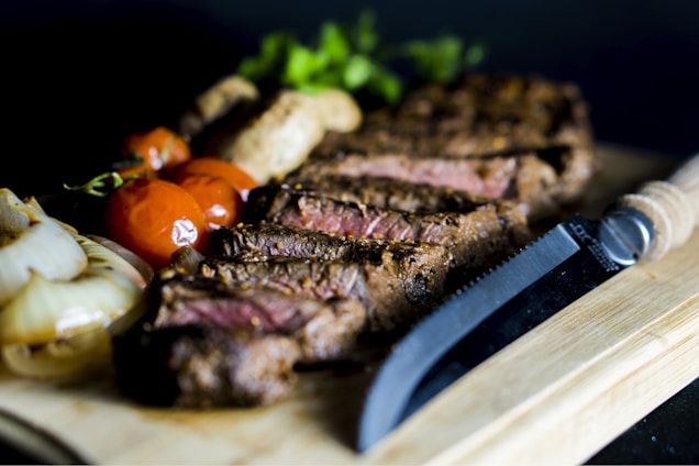 A sizzling steak on a wooden board garnished with fresh herbs and a side of roasted vegetables.