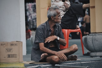 man wearing grey shirt sitting on sidewalk