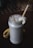 A creamy banana smoothie served in a glass jar with frothy texture on top. A slice of banana is placed on the rim of the jar, and a bamboo straw is inserted. Another banana lies on the dark surface beside the jar.