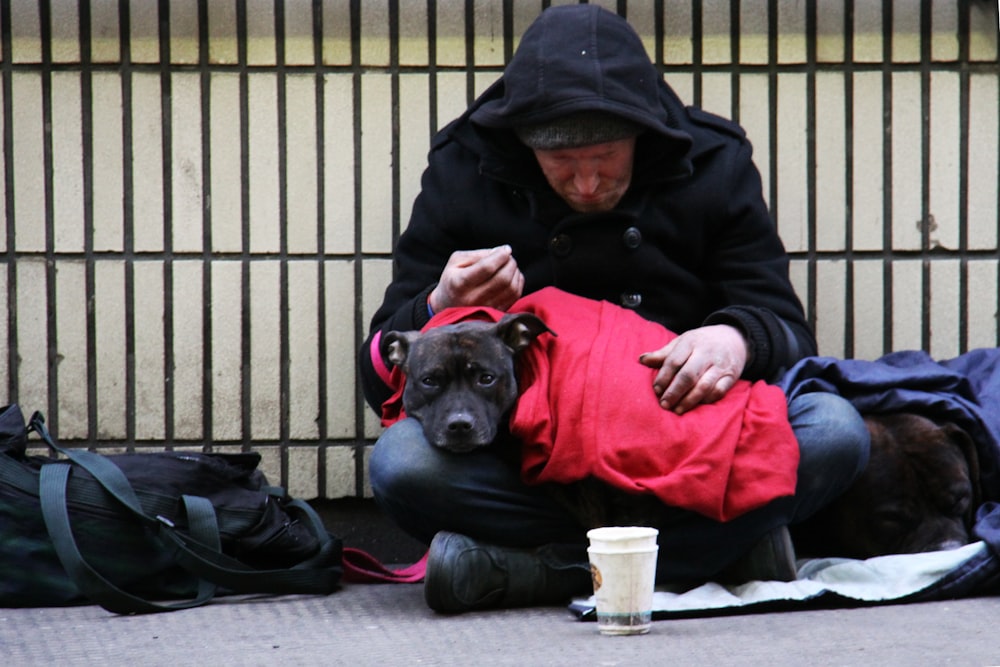 dog on top of person's lap while sitting on ground at daytime