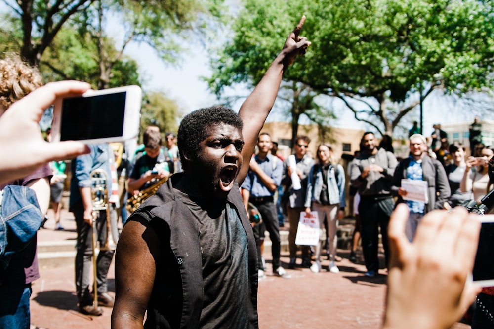 man raising his left hand while surrounded with crowd at daytime