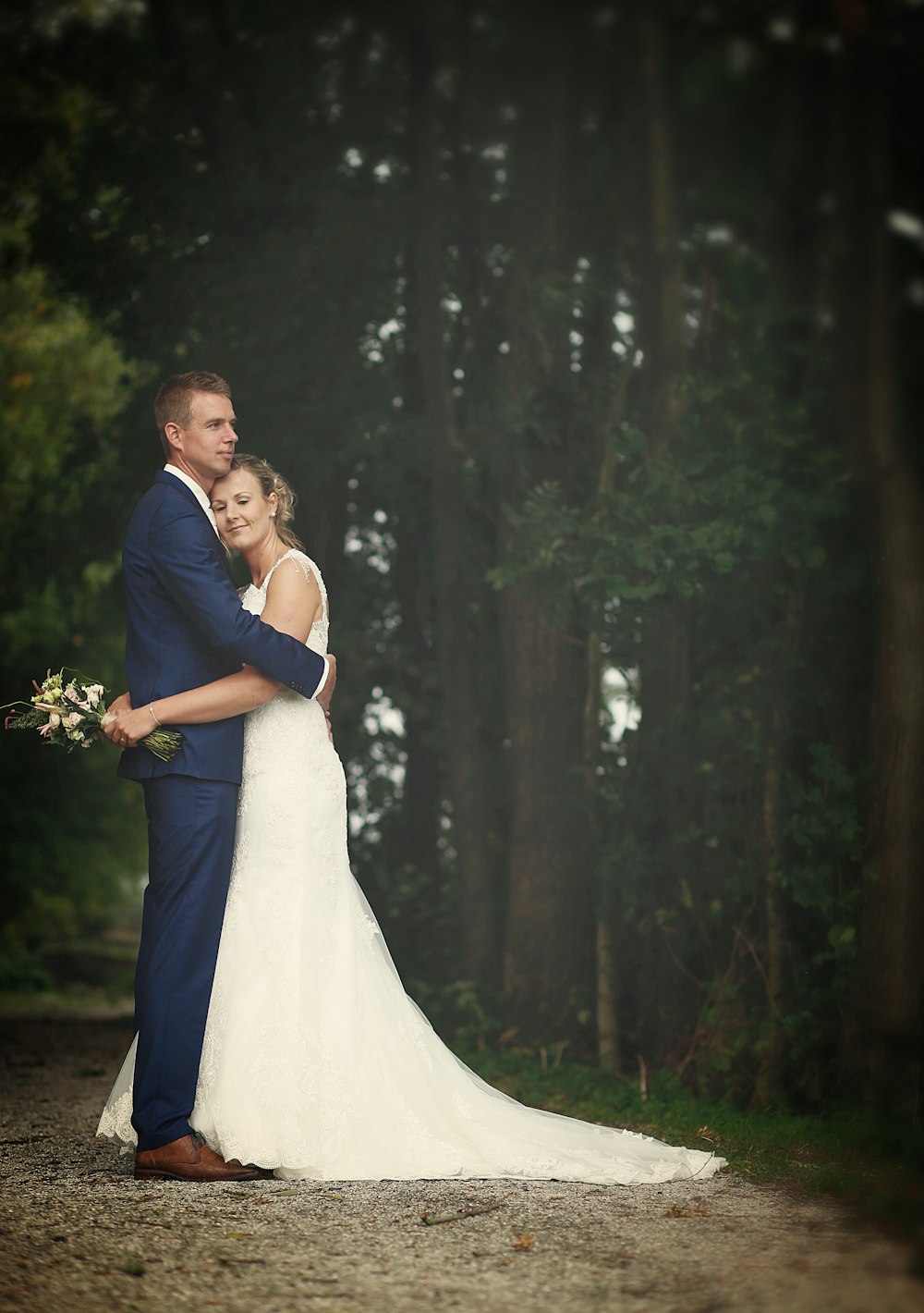 man and woman in wedding attire hugging in the forest