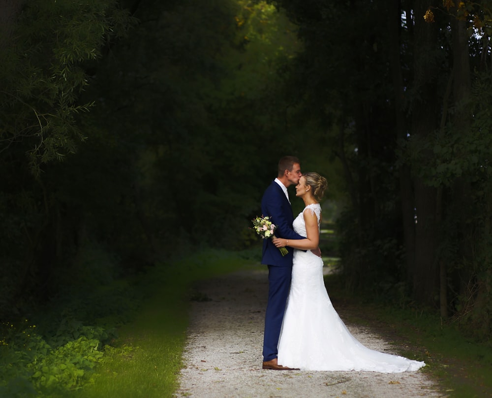 man kissing a woman's forehead while standing between trees during daytime