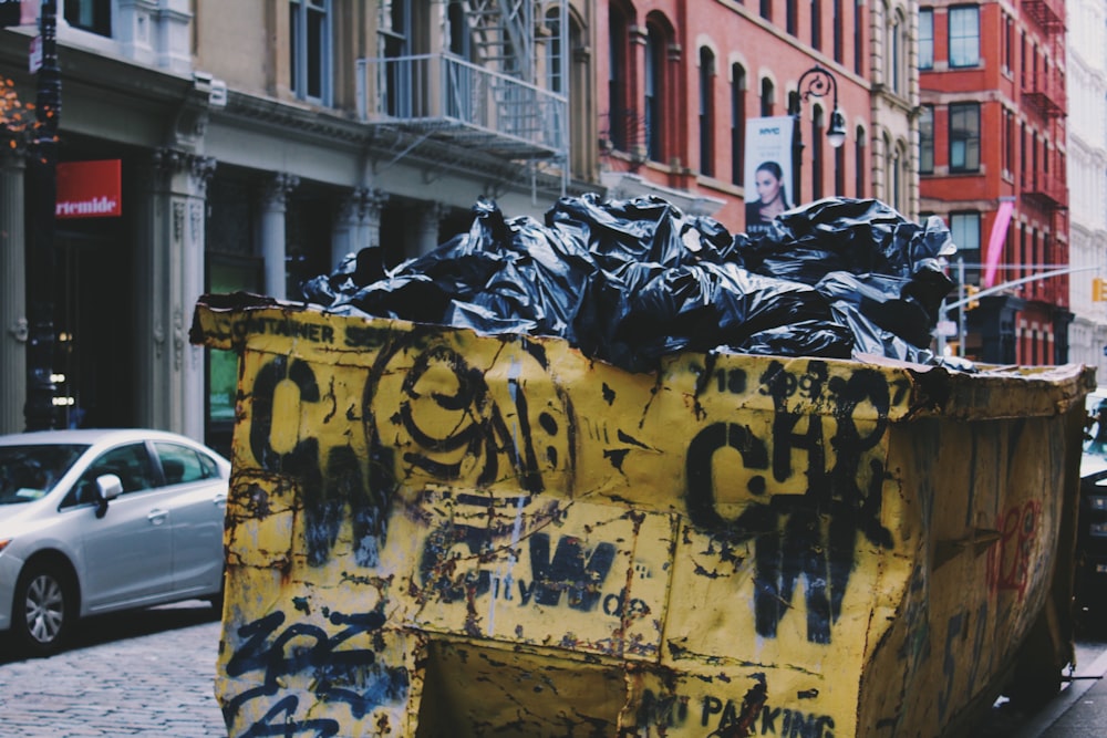 yellow garbage container near silver sedan during daytime