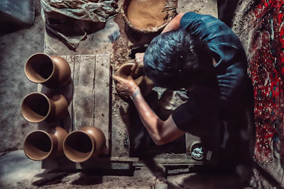 Artisan hands shaping soft clay on the wheel, surrounded by pots in various stages of creation.