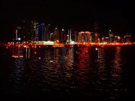 A vibrant city skyline at sunset with colorful lights reflecting on the water.