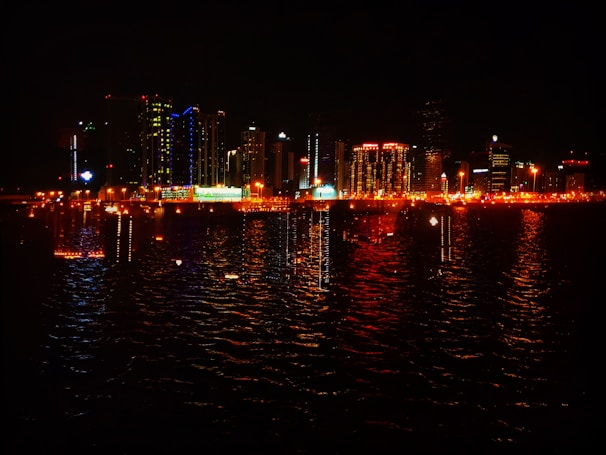 A vibrant night skyline of New York City with glowing skyscrapers reflecting in the Hudson River.
