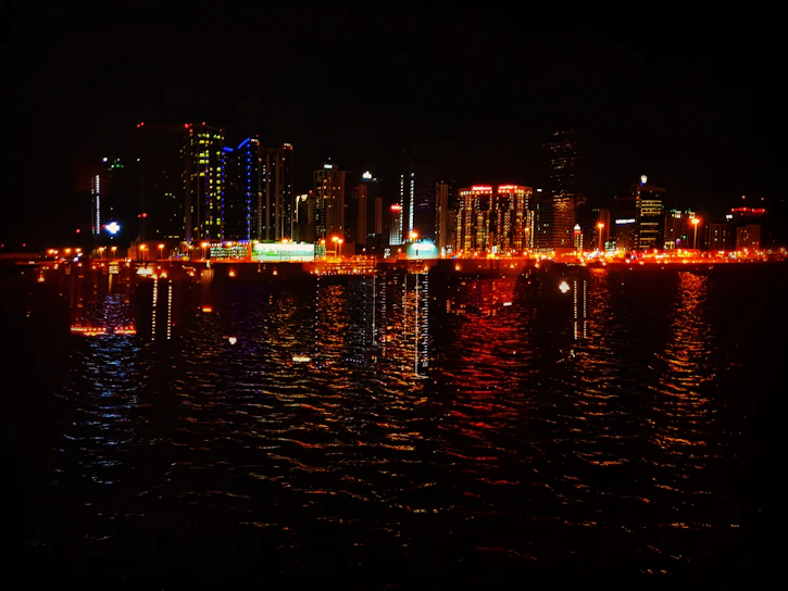 A vibrant city skyline at sunset with colorful lights reflecting on the water.