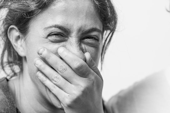 A person with tousled hair is covering their mouth with their hand while their eyes are squinting, suggesting amusement or laughter. The focus is on the expressive face, emphasizing the lines and features.
