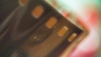 An abstract close-up image of a film strip with visible sprocket holes. The background is blurred, featuring muted colors and soft focus.