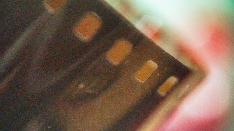 An abstract close-up image of a film strip with visible sprocket holes. The background is blurred, featuring muted colors and soft focus.