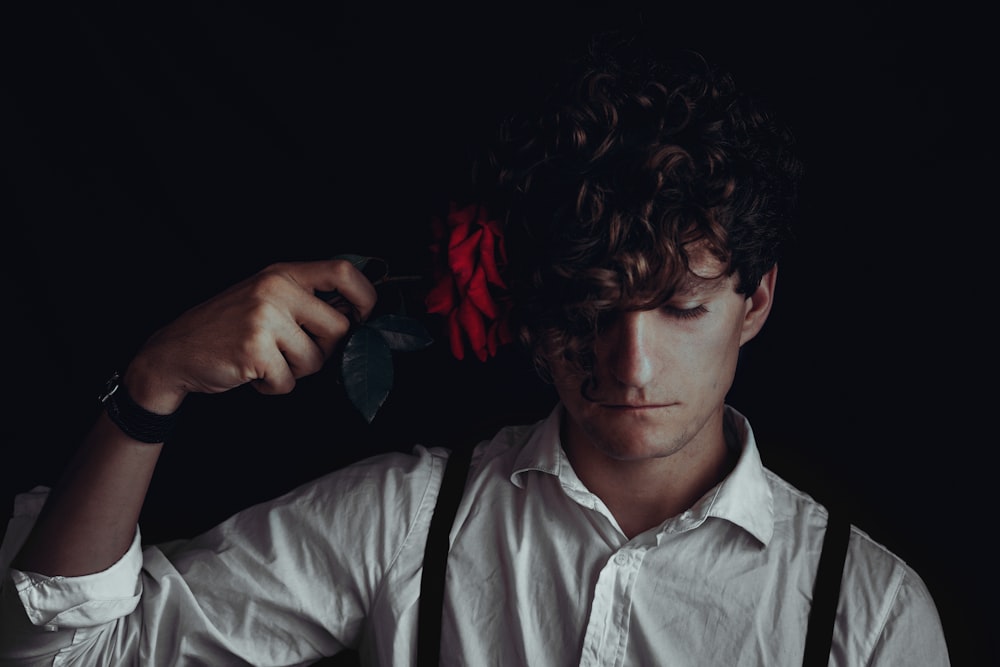 man in white dress shirt holds red flower