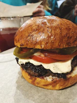 Close-up of a juicy burger with melted cheese, jalapeños, and caramelized onions drizzled with smoky adobo sauce.