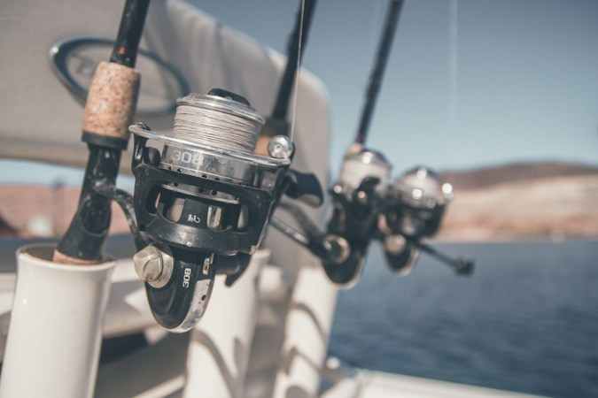 Spinning reels on rods standing in white rod holders on a boat, open water and a dry hillside blurred behind