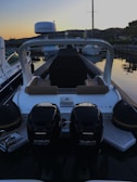 A motorboat is docked at a marina during sunset. The boat has two powerful outboard engines labeled Verado 350. The seating area features brown cushions, and a Garmin device is mounted overhead. Surrounding the boat are other vessels and hills in the background, creating a serene evening atmosphere.