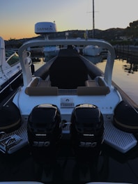 A motorboat is docked at a marina during sunset. The boat has two powerful outboard engines labeled Verado 350. The seating area features brown cushions, and a Garmin device is mounted overhead. Surrounding the boat are other vessels and hills in the background, creating a serene evening atmosphere.