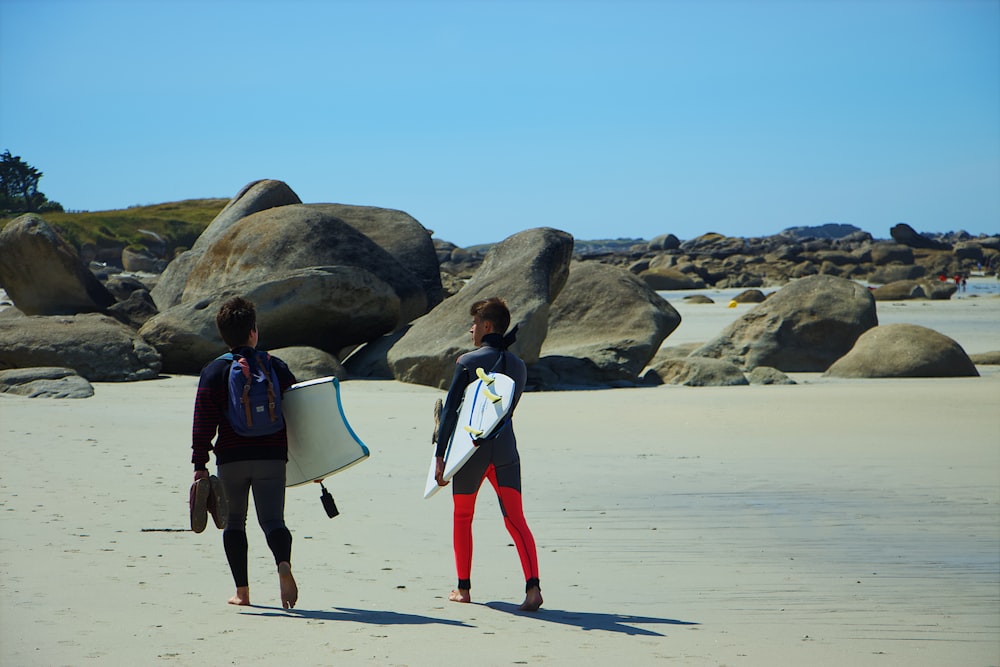 deux personnes avec des planches de surf marchant sur le bord de la mer