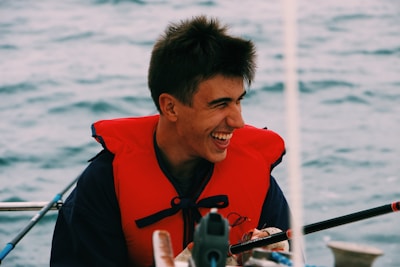 Smiling instructor helping a child put on a life jacket before a sailing lesson.