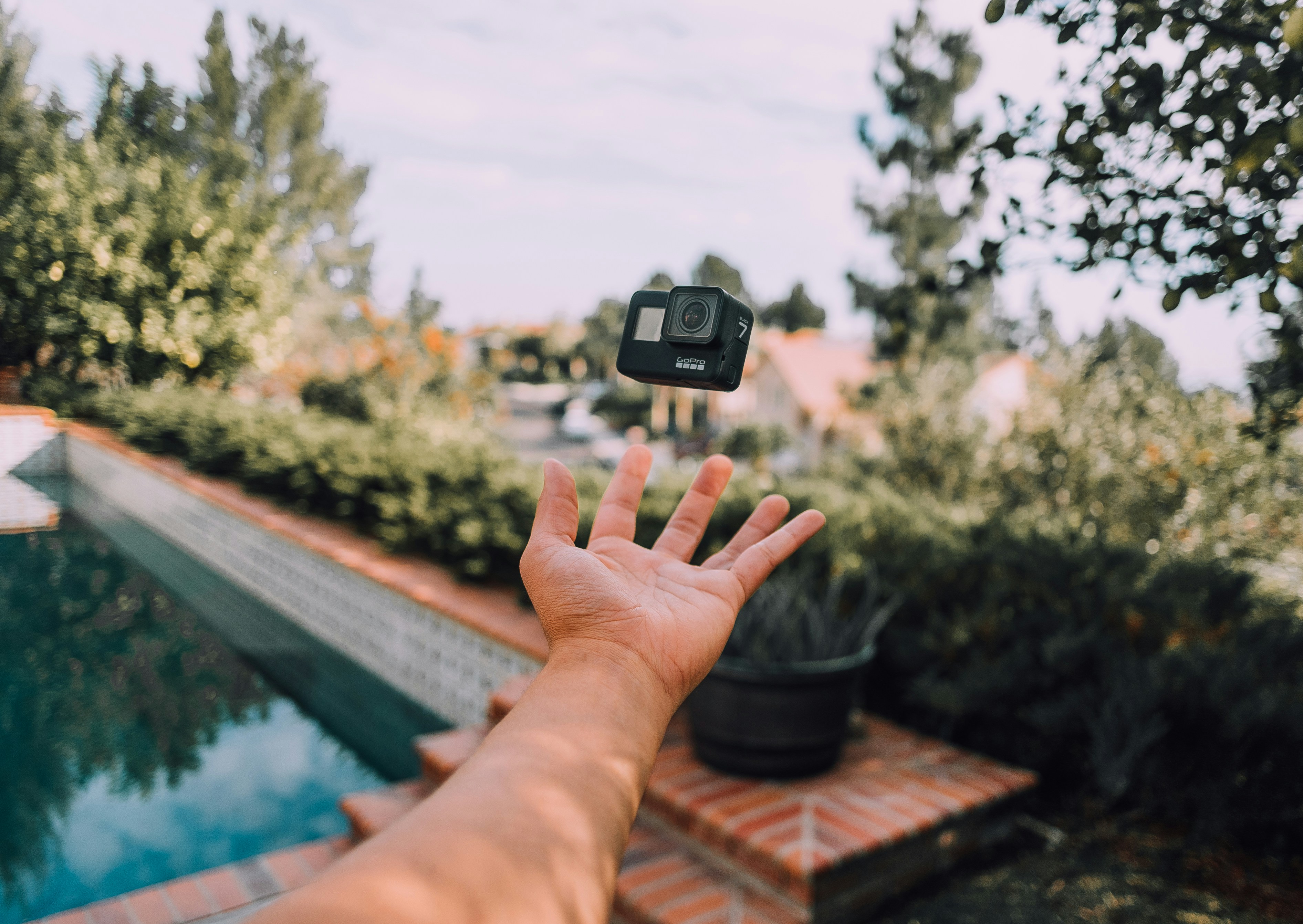 A person tosses a GoPro Camera mid-air in front of a swimming pool, creating a video about how to add music in GoPro Quik.