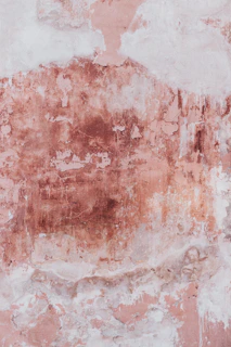 A weathered wall with peeling pink paint and exposed plaster in Wrocław, Poland